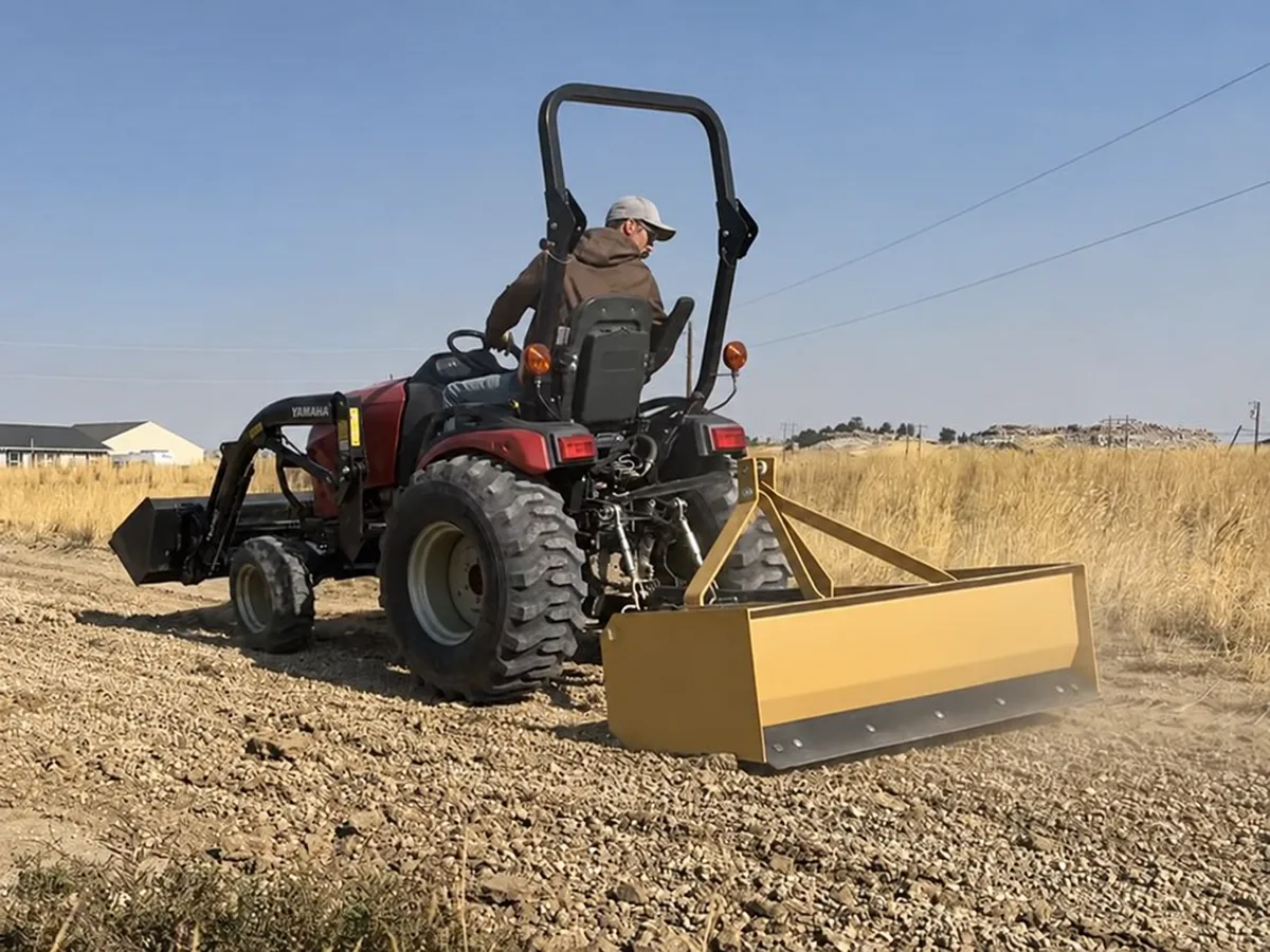Tractor-mounted box blade grading a track