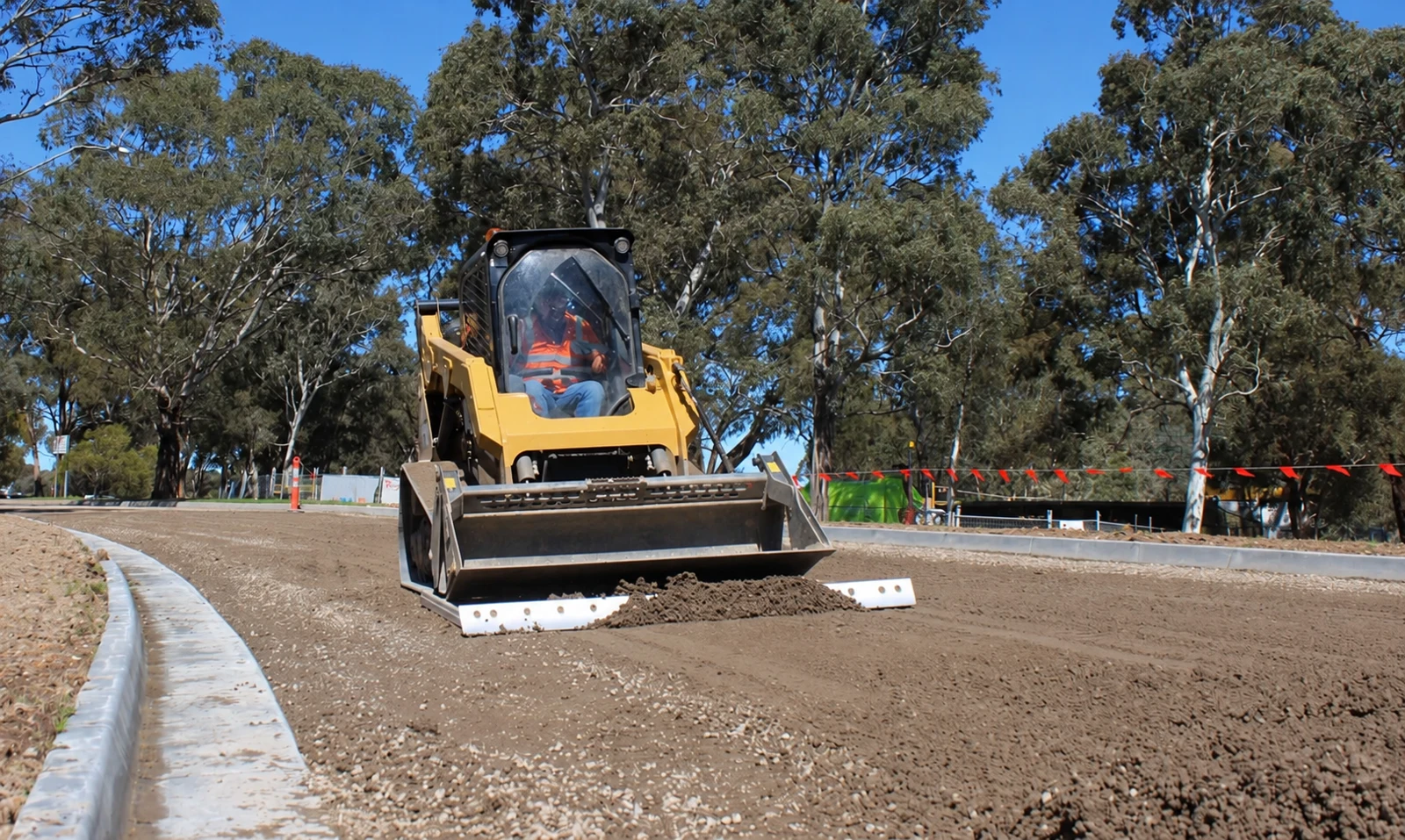 Wheeled skid-steer loader levelling a road surface