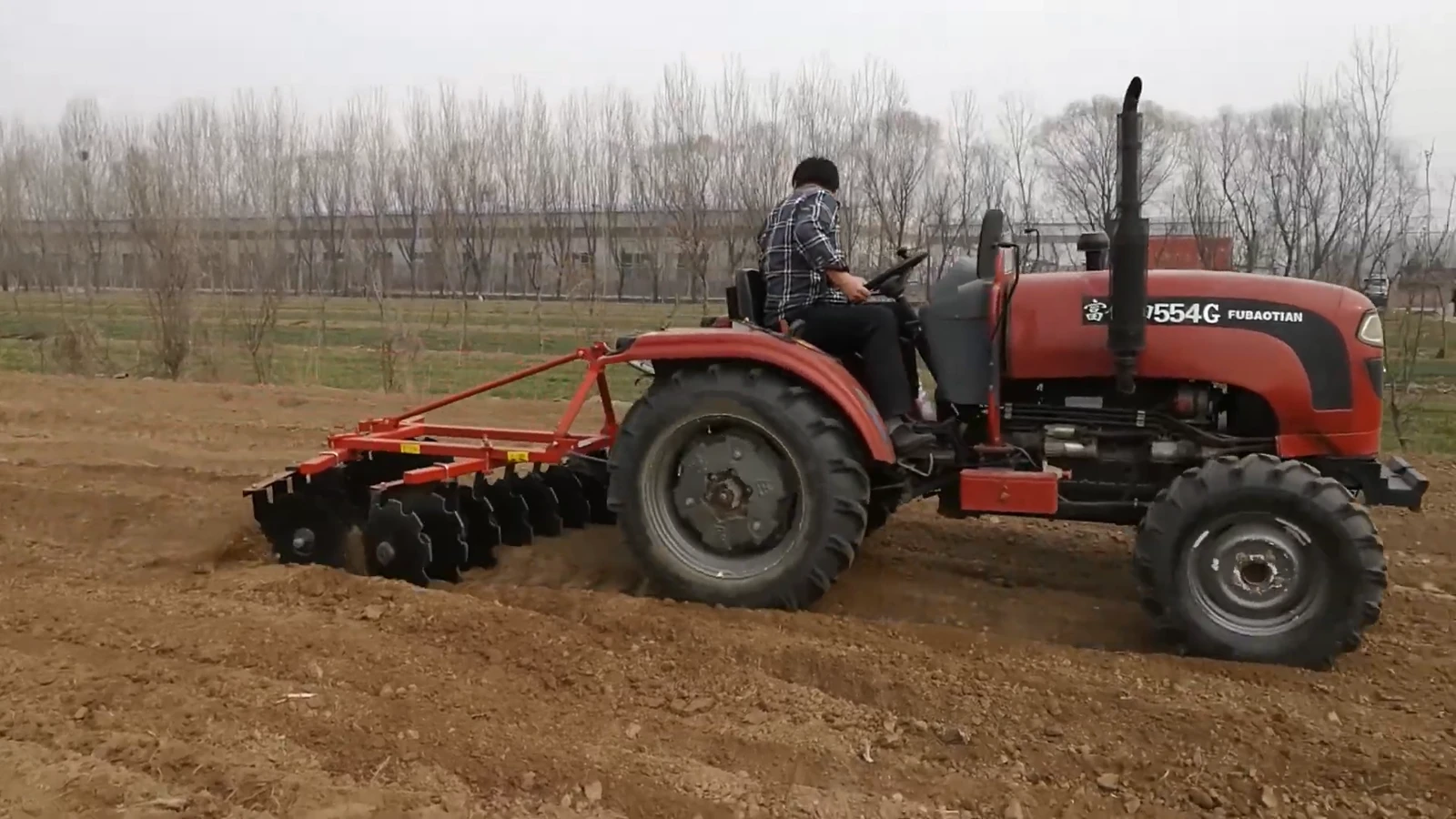Tractor drawing a mounted disc harrow through cultivated soil with visible concave disc gangs