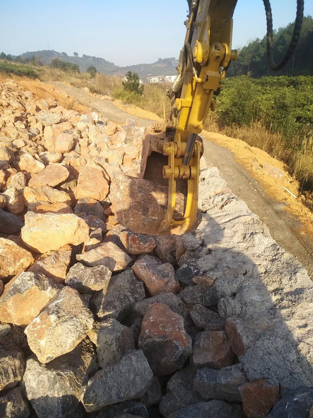 Excavator hydraulic thumb and bucket gripping a large rock at a work site