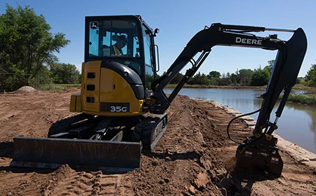 Excavator-mounted hydraulic plate compactor working on prepared soil