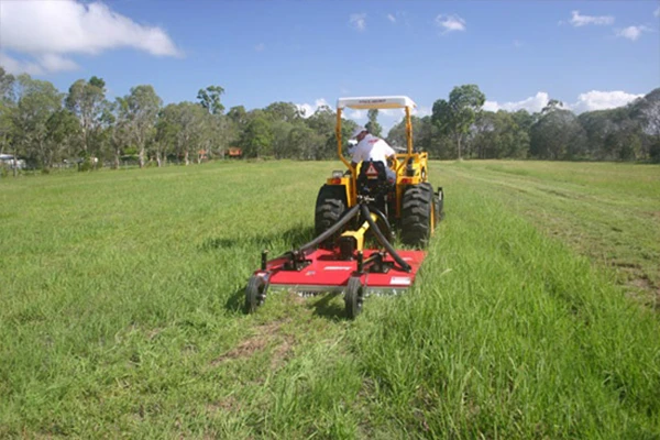Tractor-mounted rotary cutter mowing grass with a vertical-axis cutting deck and rear support wheel